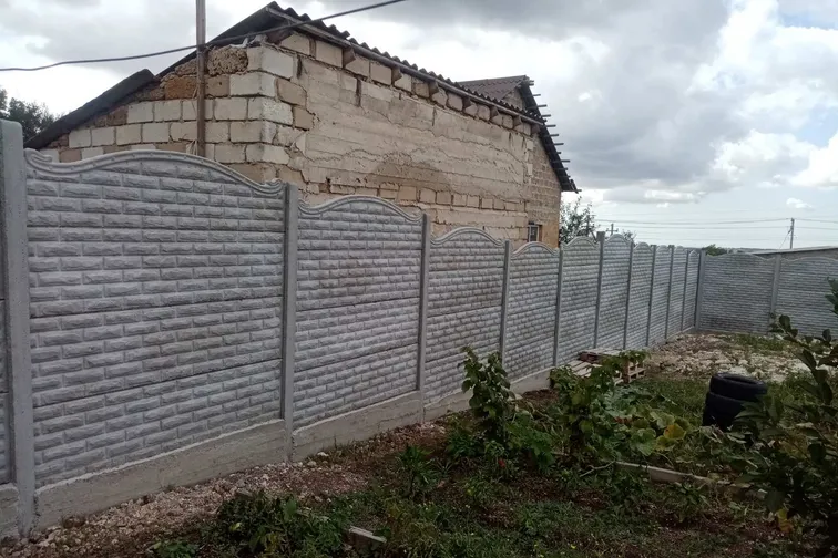 Еврозабор с волнистым верхом у дома из белого камня